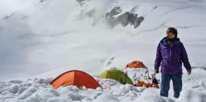 man standing aside tents in a snowy mountain