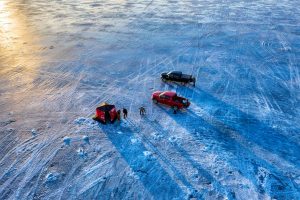 ice fishing with shelters, two men, and two cars